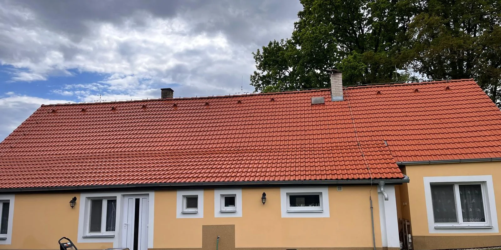 Střecha přízemního domu se žlutou fasádou před a po čištění na Svaté Anně v Táboře — po čištění