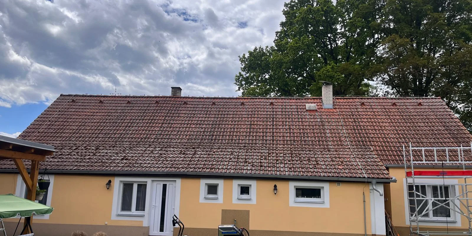 Střecha přízemního domu se žlutou fasádou před a po čištění na Svaté Anně v Táboře — před čištěním